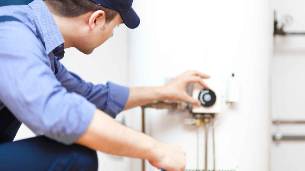 A technician adjusting the thermostat on a water heater system indoors.