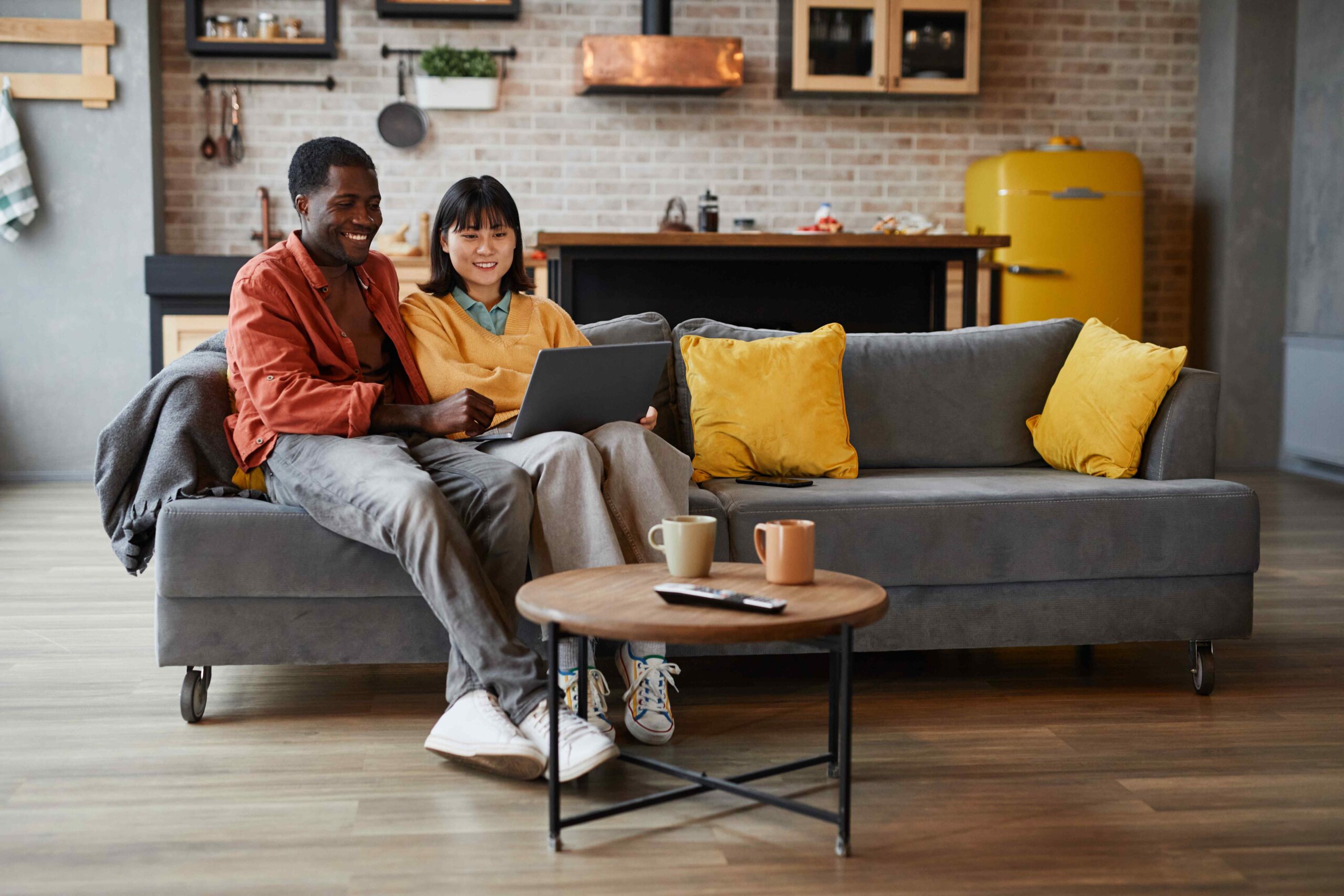 Two people sitting on a sofa in Jackson, looking at a laptop screen with coffee cups on the table in front of them.