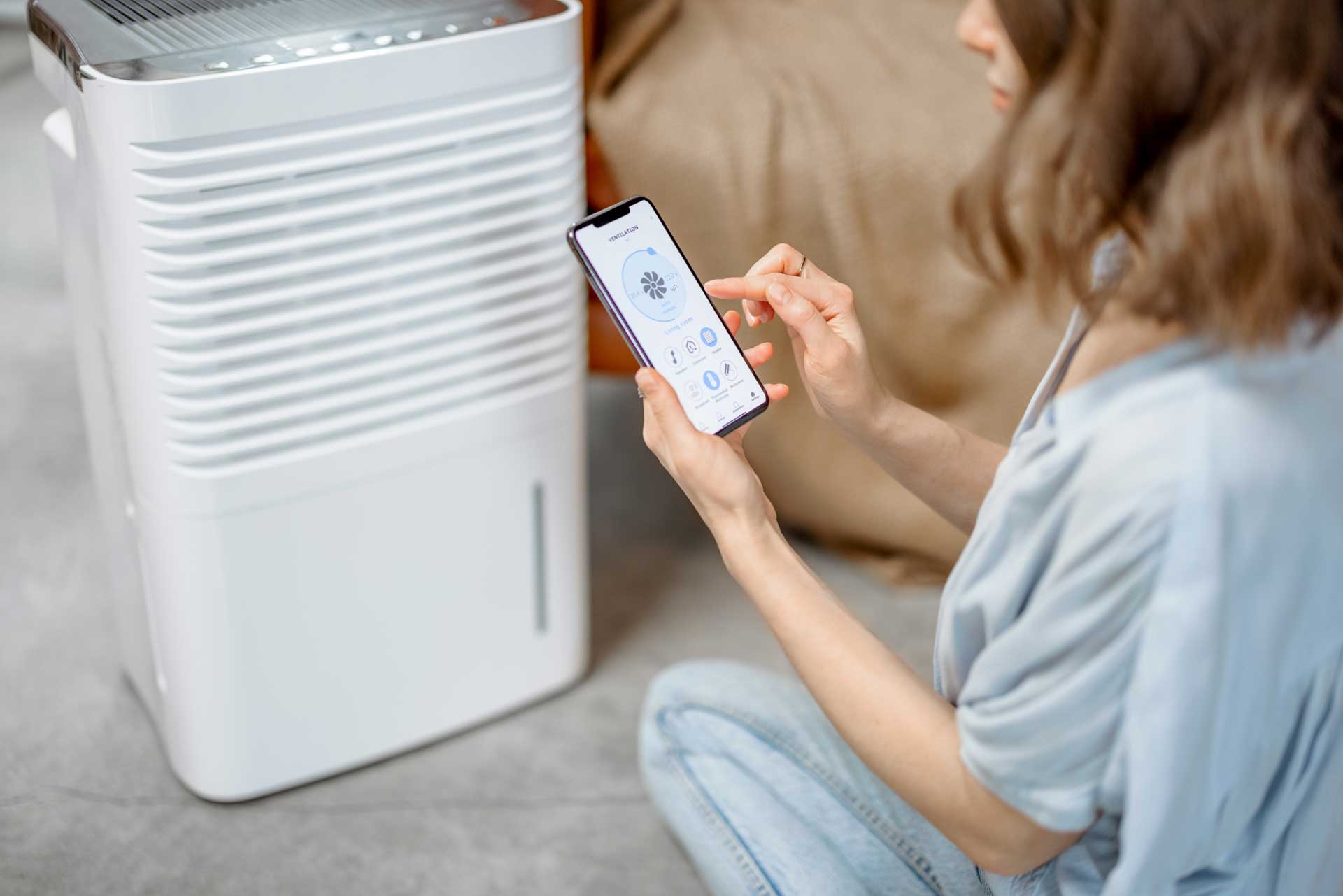 Woman using a smartphone to control a smart water softening system in a modern home setting.