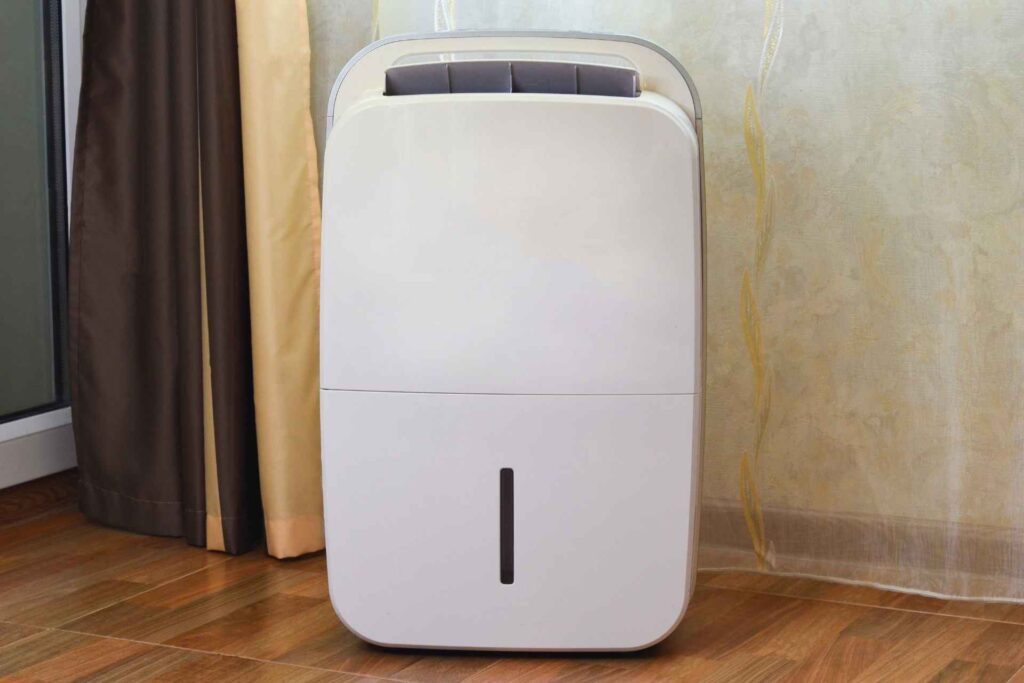 A portable air conditioner with water filtration positioned on a hardwood floor beside curtains in a room.