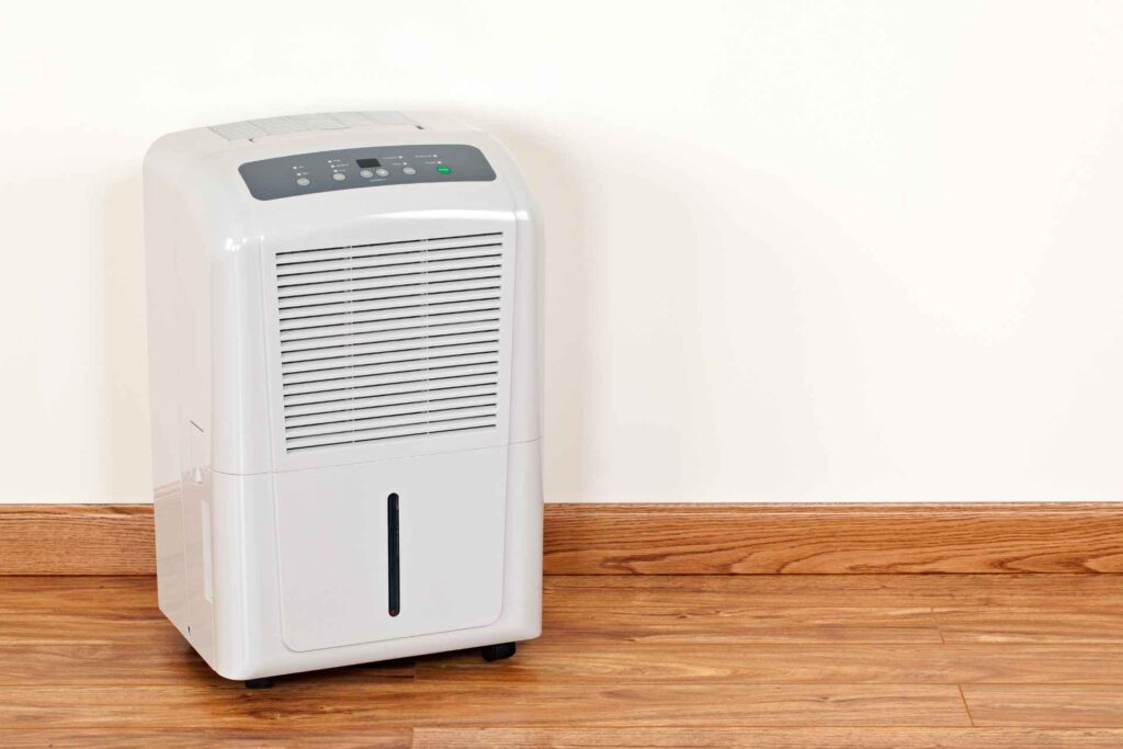 Portable air conditioner with water filtration system standing on a hardwood floor against a plain wall, control panel visible on the top.