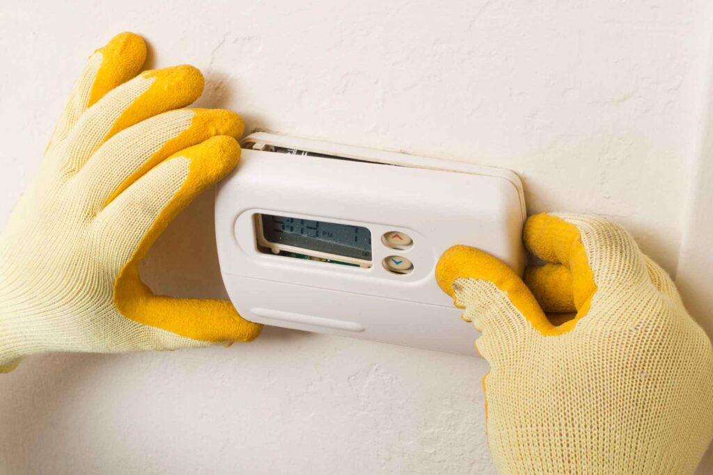 Hands in yellow gloves adjusting a water filtration system on a white wall.
