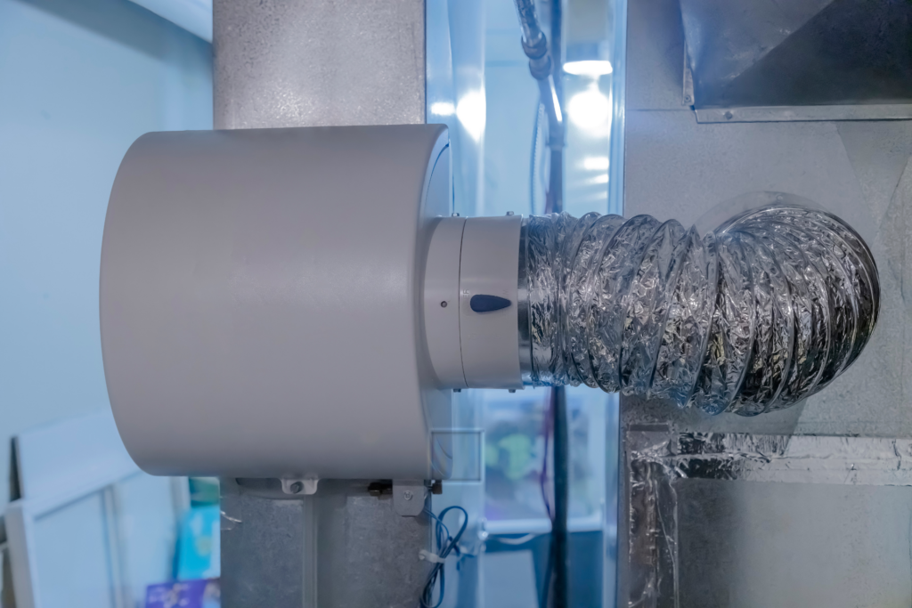 Industrial air duct connected to a large cylindrical water filtration unit mounted on a wall in a facility.