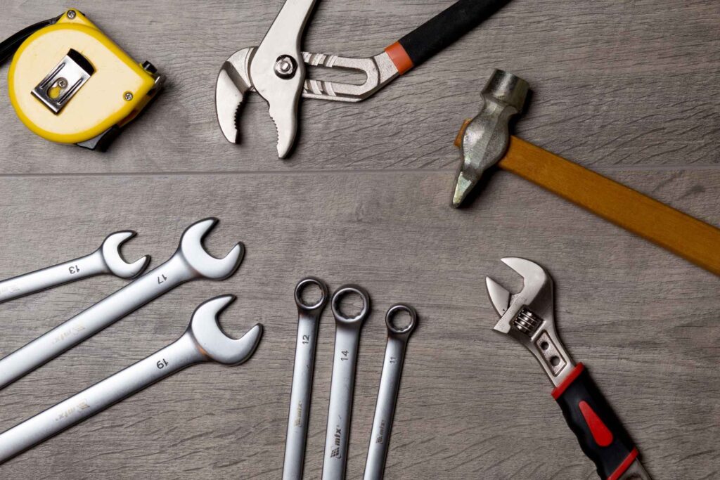 Assorted hand tools including wrenches, pliers, a hammer, and a tape measure arranged on a wooden surface for water filtration system maintenance.