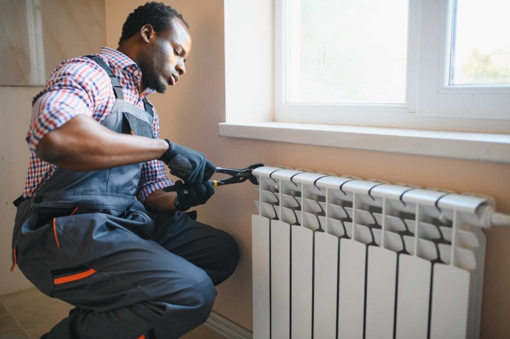 A man using pliers to fix a water filtration system beside a window. He is focused on his work, wearing a plaid shirt and a tool belt.