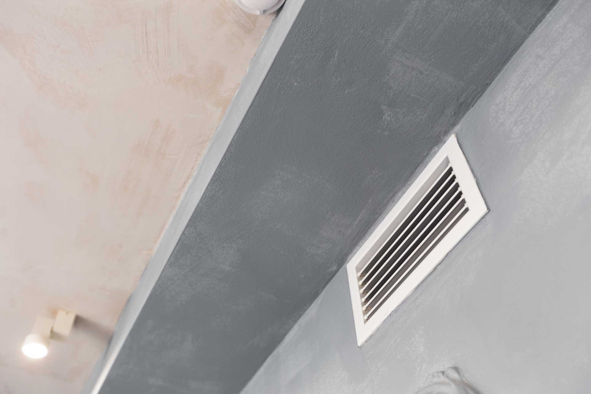 A ceiling-mounted hvac vent on a grey, textured surface with tub replacement and recessed lighting visible in the background.