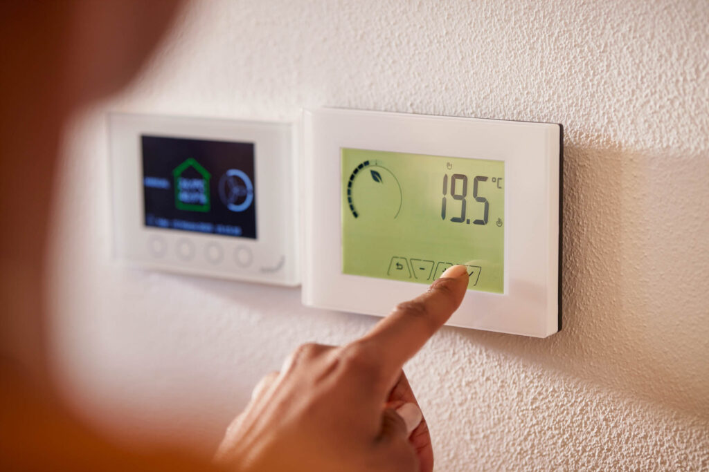 A person adjusting a digital thermostat set to 19.5°c on a wall.