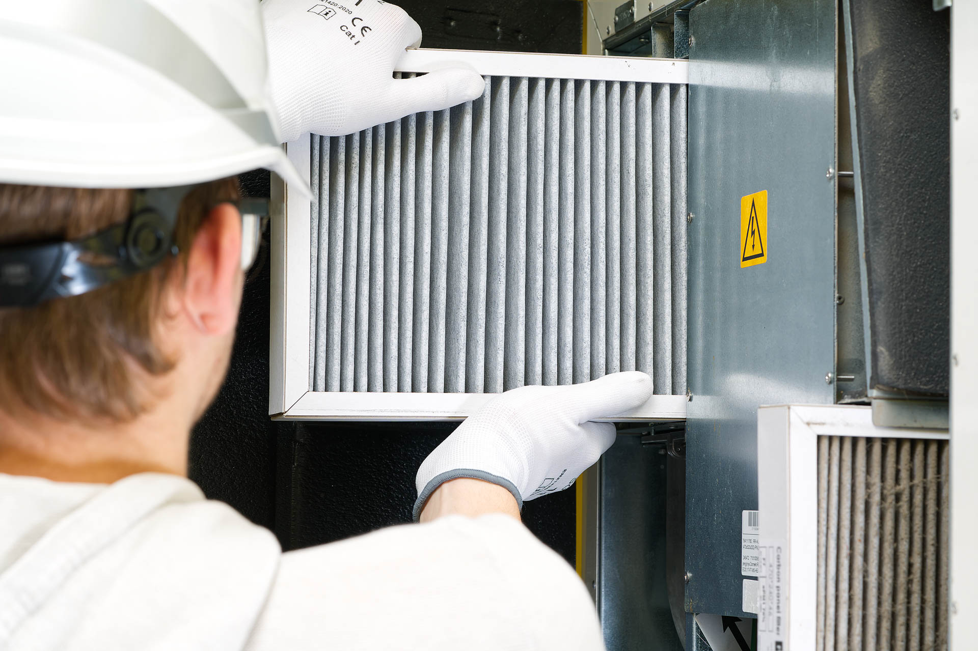 A technician wearing safety gloves and a helmet is inspecting or changing an air filter in a large hvac unit.
