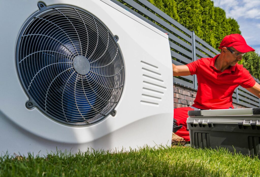 A technician in a red uniform servicing an outdoor air conditioning and water filtration unit on a sunny day.