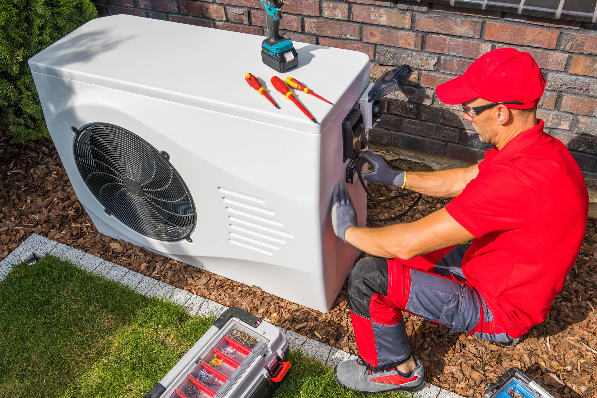 A technician in red uniform servicing an outdoor water filtration unit with tools nearby.