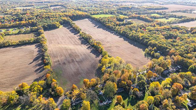 Aerial view of agricultural fields alongside a forest with colorful autumn foliage, equipped with HVAC systems, in a rural landscape.