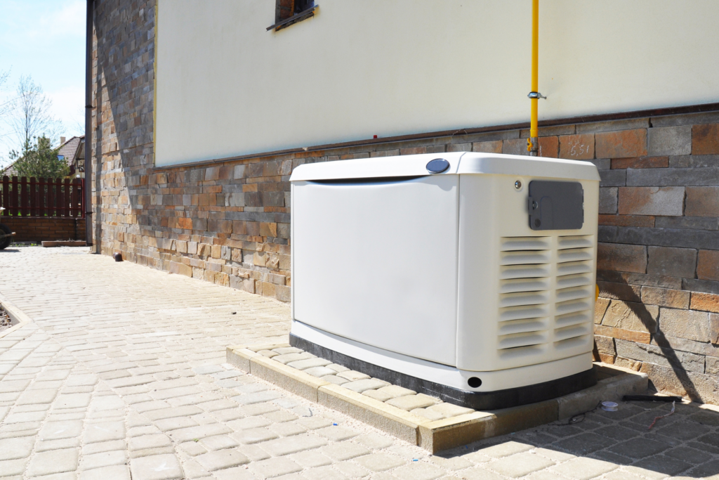 A white standby generator installed on a concrete pad outside a brick and stucco building. The generator is connected by a yellow fuel line and positioned on a paved area beside the structure, ensuring uninterrupted power for heating and cooling systems.
