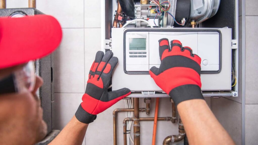 Technician in a red cap and gloves adjusts settings on a residential gas furnace's gas line control panel.