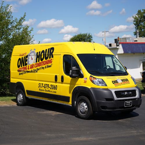 A yellow van with “One Hour Heating & Air Conditioning” branding is parked on a paved driveway near grass and trees under a sunny sky, highlighting their trusted HVAC services in the neighborhood.