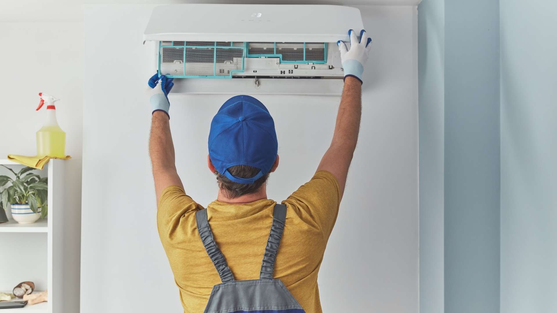 A man in a blue cap and overalls inspects an air conditioner