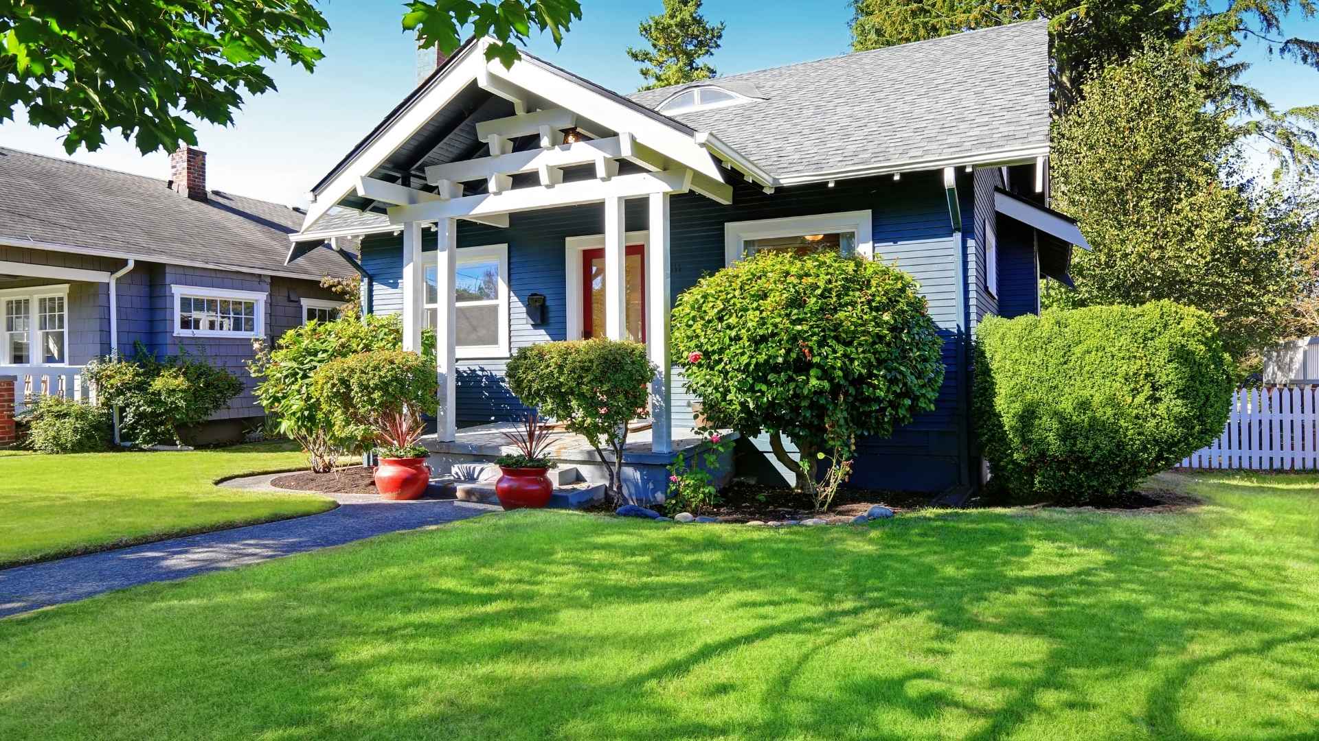 A small blue house with a porch, white trim, and red door