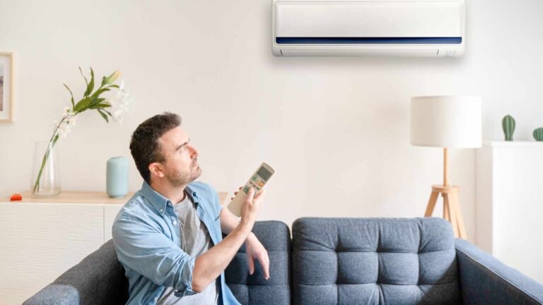 A man sitting on a blue sofa controlling the ac