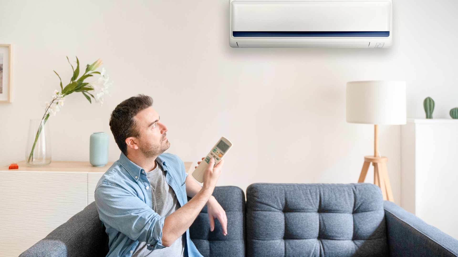 A man sitting on a blue sofa controlling the ac