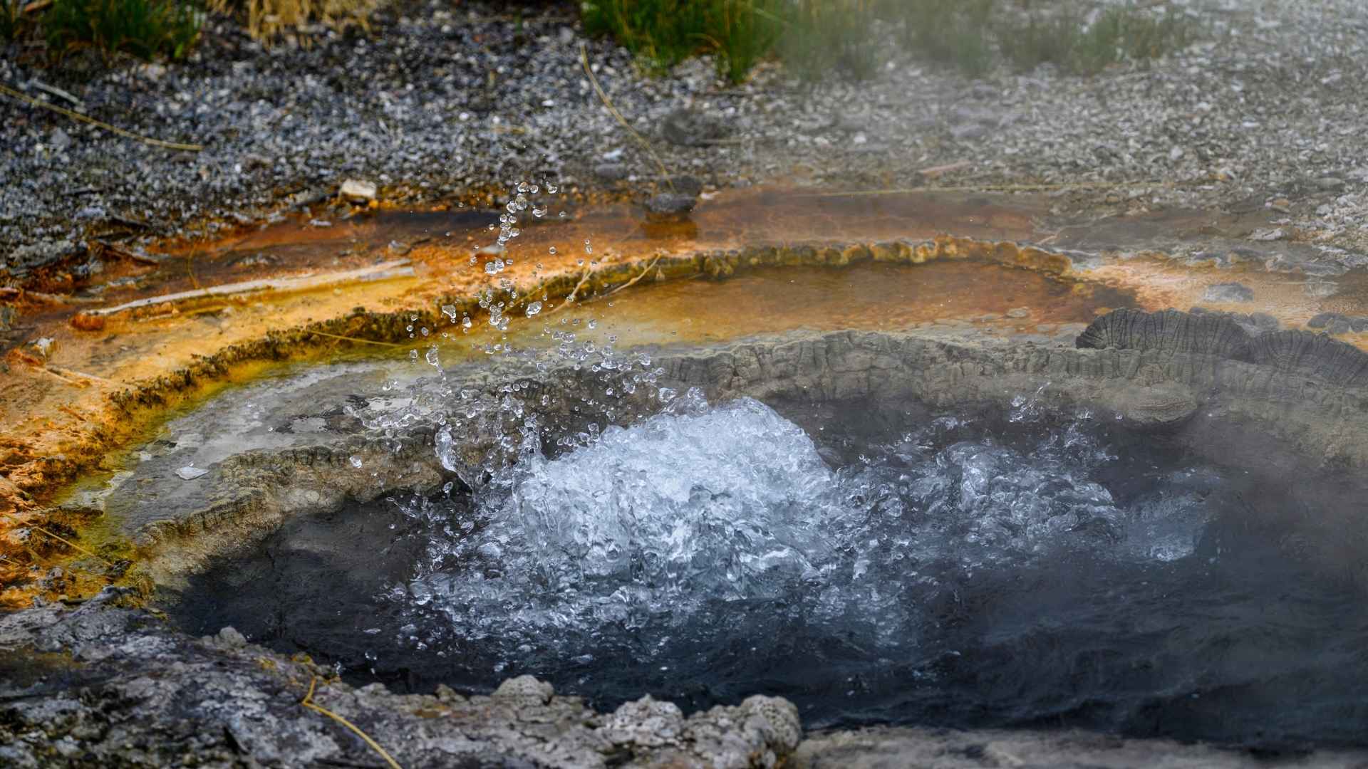 GeoThermal Heating in Michigan Hot spring water bubbles and splashes from a circular geothermal vent surrounded by mineral deposits and rocky ground.