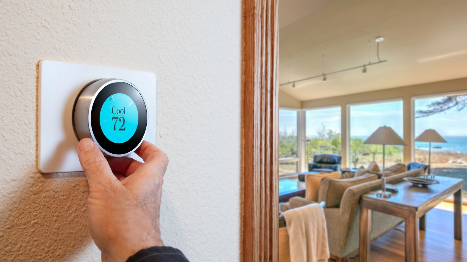 programmable thermostat A hand adjusts a smart thermostat set to 72 degrees Fahrenheit on a wall near a bright living room with large windows overlooking a scenic outdoor view.