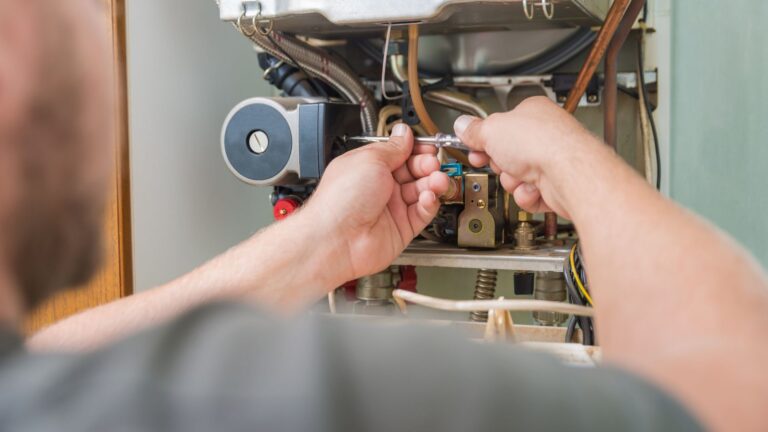 furnace replacement A person uses a wrench to repair or adjust an exposed boiler or heating system.