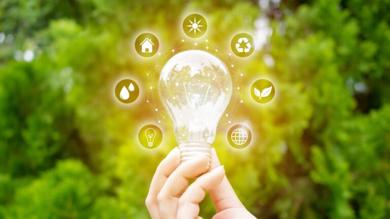 energy-efficient heating in michigan A hand holds a glowing lightbulb with various eco-friendly and sustainability icons surrounding it, set against a blurred green background.