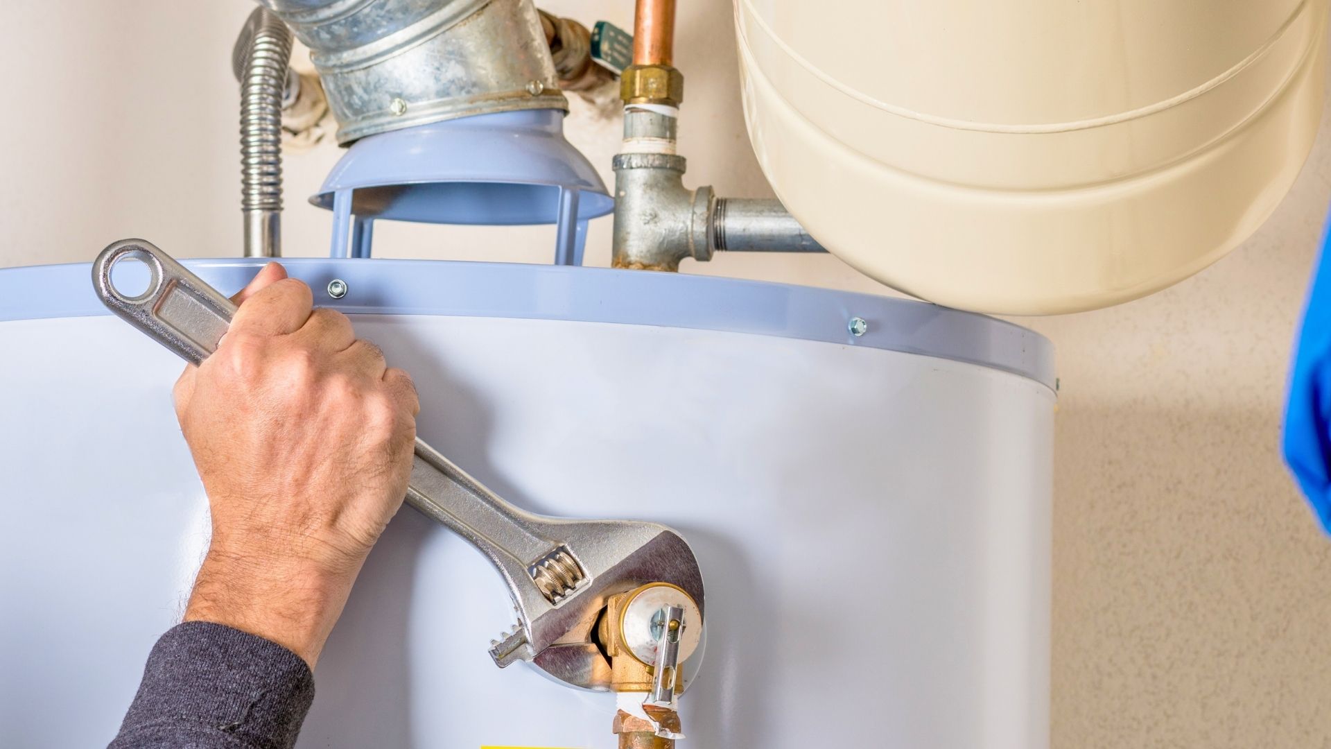 heating maintenance in michigan A person uses a large adjustable wrench to tighten a pipe fitting on a water heater.