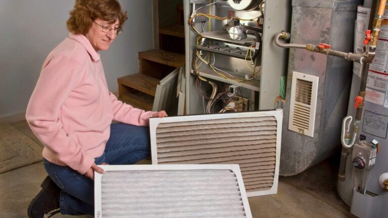 home air filtration in michigan A person kneels by an open furnace, comparing a clean air filter with a dirty, used one.