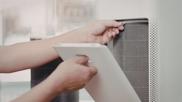 A person is changing the filter of an air purifier, holding the front cover.