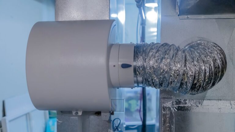 A close-up view of an air duct system with a flexible foil ventilation hose connected to a cylindrical device on a wall.